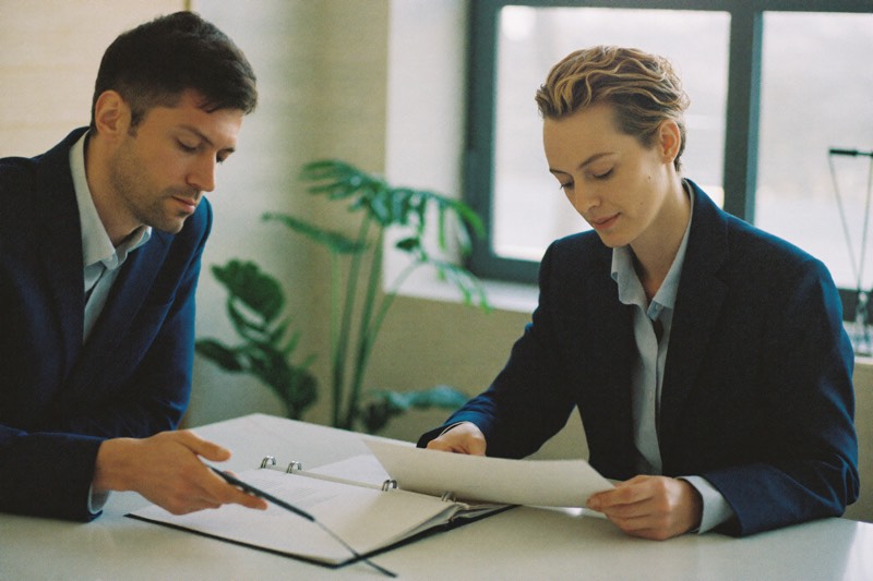 Two professionals review a binder of documents together at a desk.