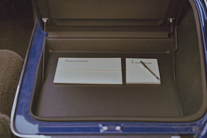 An open glovebox holding an envelope, a notepad, and a pen.