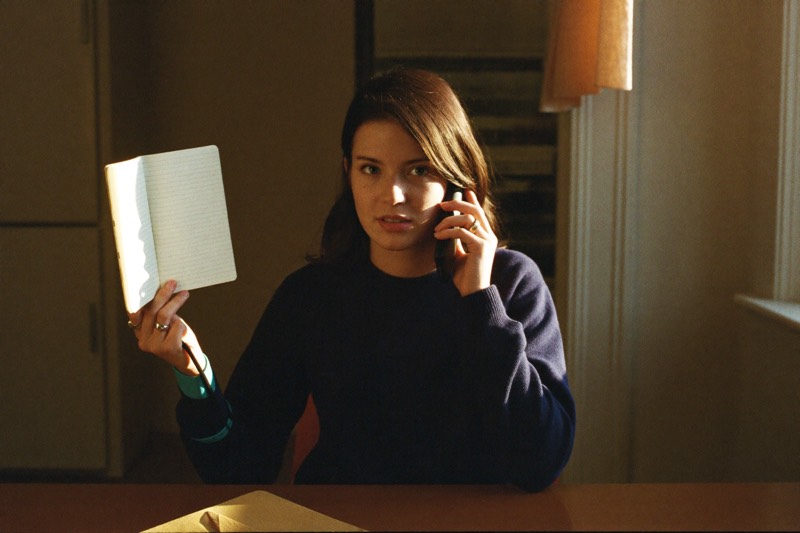 A person writes in a notebook at a warm kitchen table.