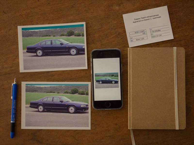 Printed photos of a car beside a phone, notebook, and insurance card.
