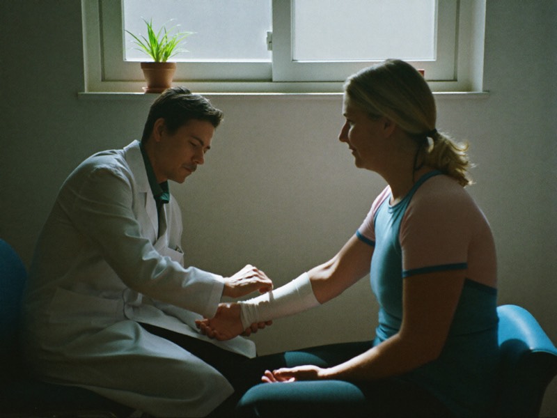 A doctor gently wraps a patient's wrist in a calm exam room.