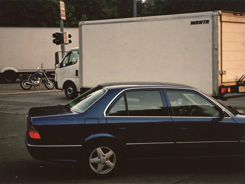 A quiet intersection with a car, a box truck, and a parked motorcycle.